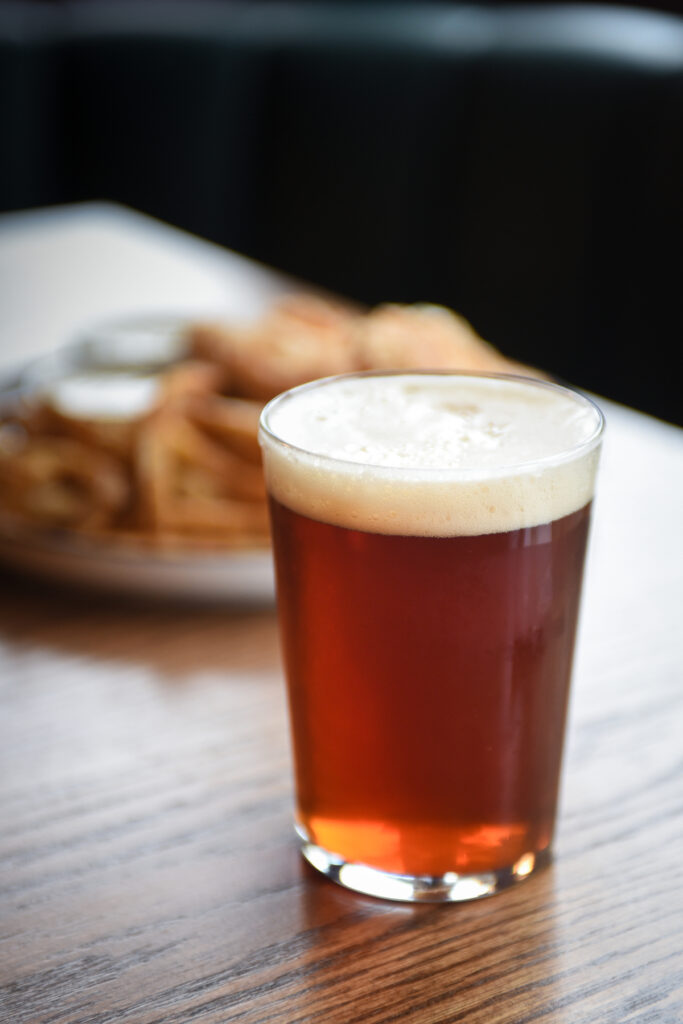 Craft beer in glass with fish and chips blurred in background on table with window light